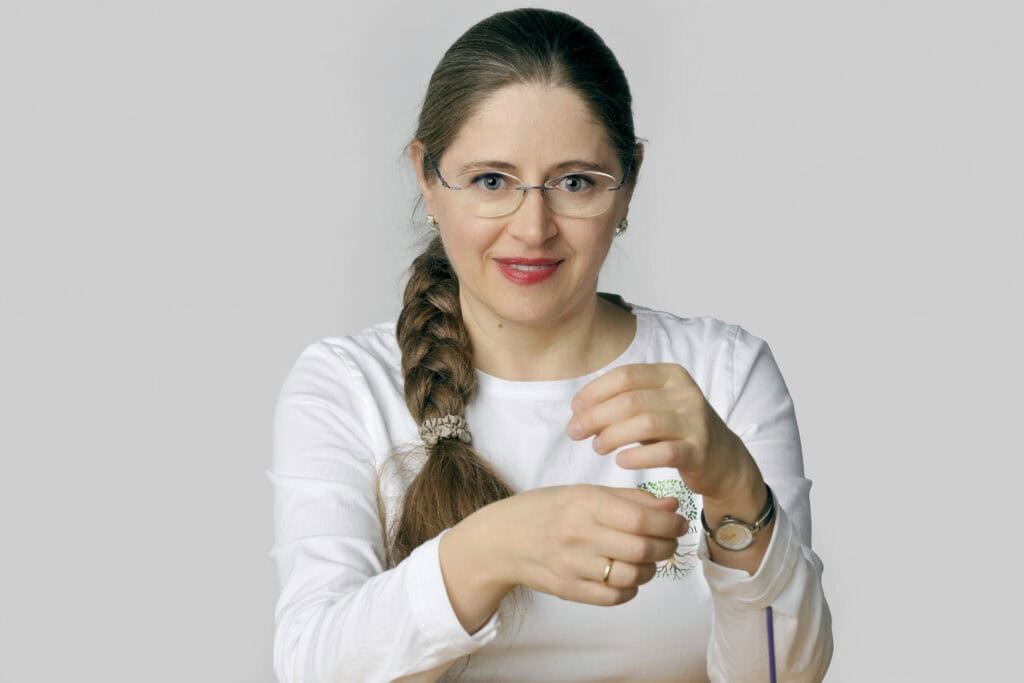 Frau mit Brille und langem Haar, die Kräuter hält und lächelt, symbolisiert Naturheilkunde und gesunde Ernährung. Perfekt für Themen rund um Kräuter, Gesundheit und Naturmedizin.