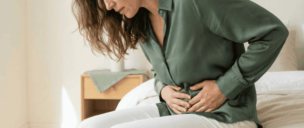 Frau hält sich schmerzhaft den Unterbauch, Anzeichen für Beschwerden oder Erkrankungen im unteren Bauchbereich.