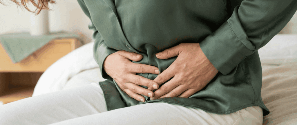 Frau hält sich den Magen, zeigt Beschwerden durch Verdauungsprobleme, sitzend auf einem Bett im Schlafzimmer.