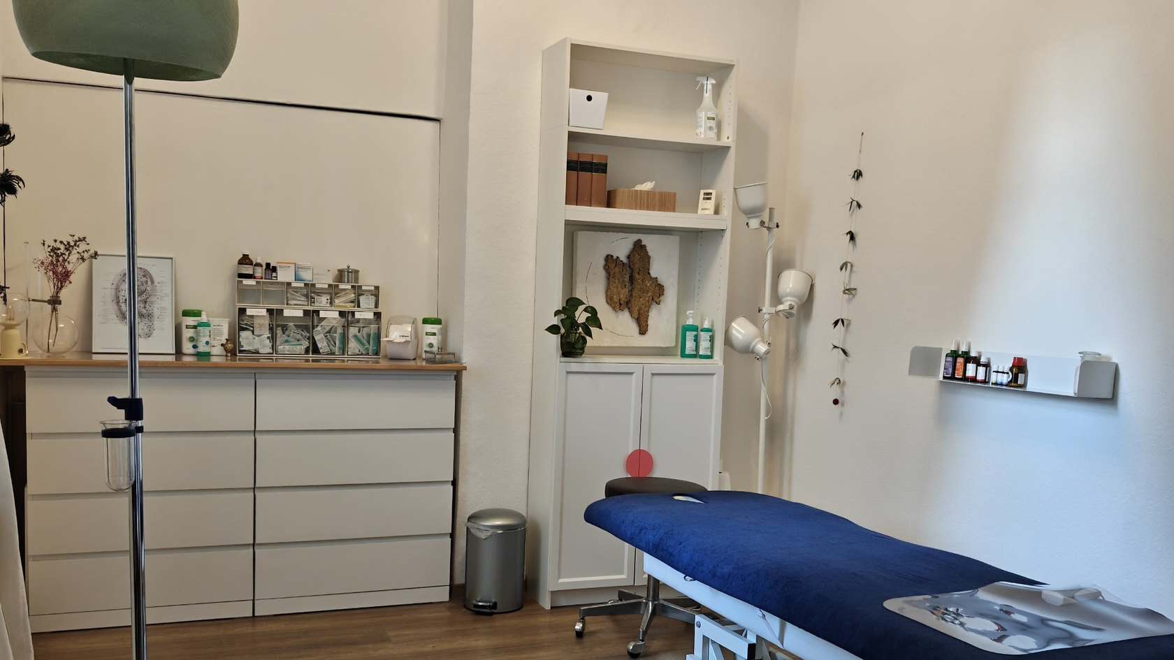 Behandlungsraum mit Behandlungsliege, medizinischen Utensilien und dekorativen Elementen in einer modernen Praxis.